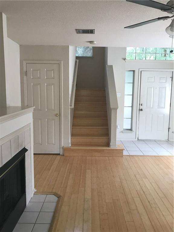 8337 Alvin High Lane Austin, TX 78729 - Photo 7 of 14 Entrance foyer featuring stairs, a ceiling fan, light wood-style flooring, a fireplace, and a textured ceiling