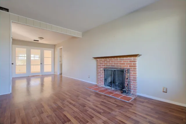 an empty room with wooden floor fireplace and windows