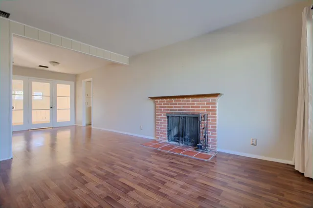 a view of an empty room with wooden floor fireplace and a window