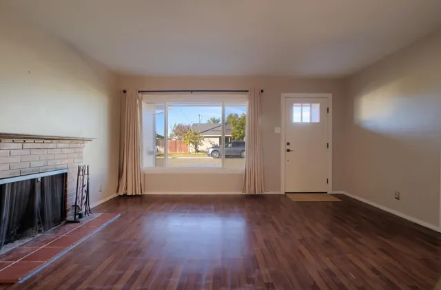 an empty room with wooden floor fireplace and windows