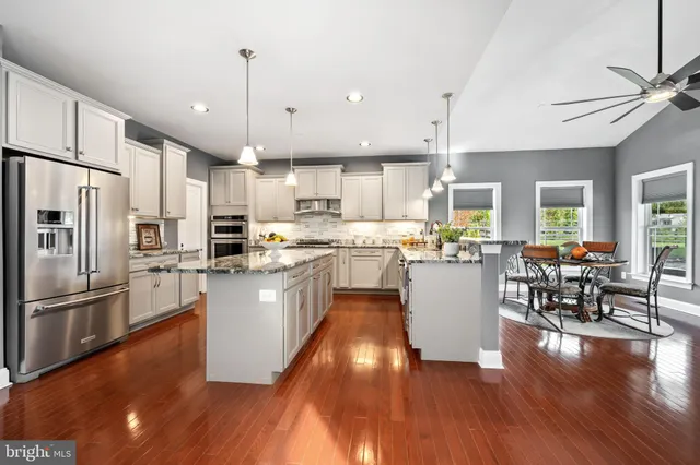 a kitchen with stainless steel appliances granite countertop a refrigerator a stove top oven a sink dishwasher a dining table and chairs with wooden floor