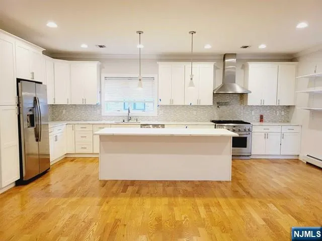 a large white kitchen with stainless steel appliances granite countertop a stove a sink a refrigerator and white cabinets with wooden floor