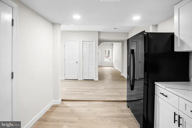 a view of a refrigerator in kitchen and an empty room with wooden floor