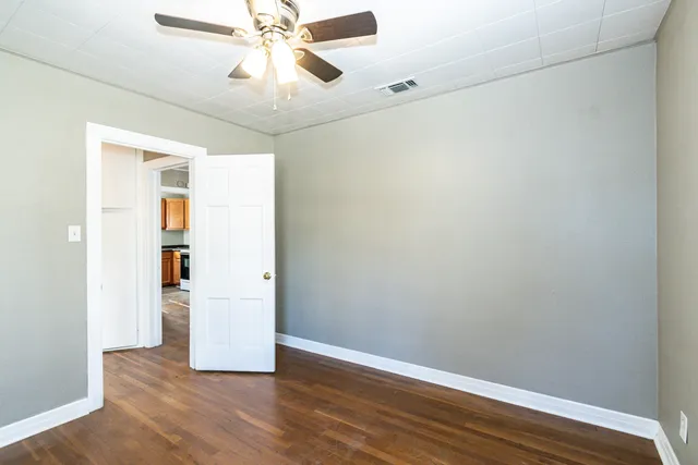 a view of an empty room with wooden floor and a ceiling fan