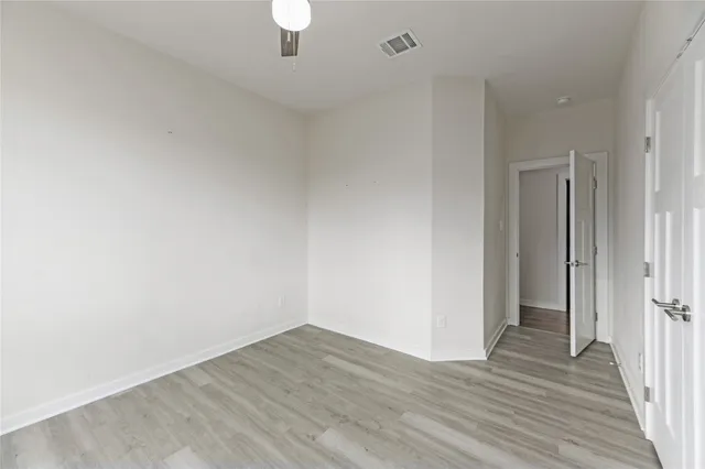 a view of an empty room with wooden floor and a ceiling fan