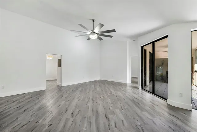 an empty room with wooden floor chandelier fan and windows