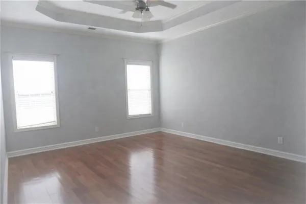 an empty room with wooden floor chandelier fan and windows