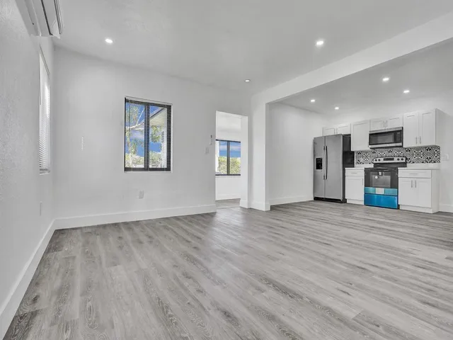 a view of empty room with wooden floor and kitchen