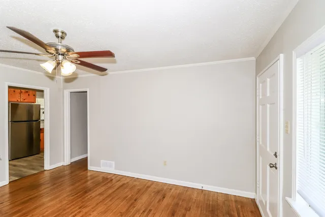 an empty room with wooden floor fan and windows