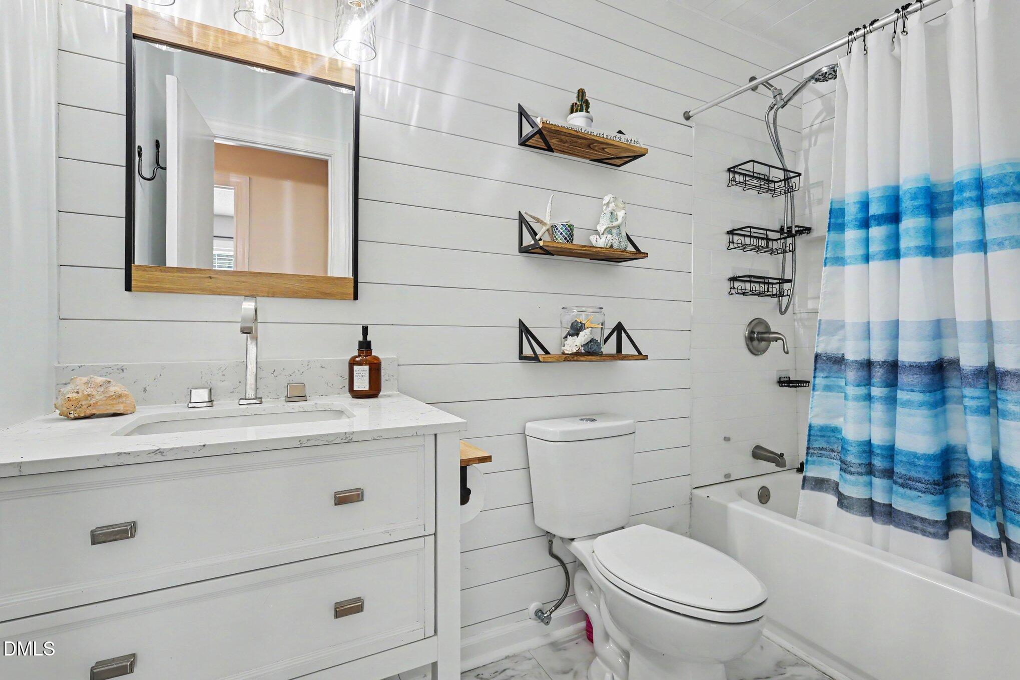 5817 Mitchell Mill Road Wake Forest, NC 27587 - Photo 22 of 34 White shiplap accent wall, white vanity with integrated sink, rectangular mirror with wood-finish frame, built-in shelving, and a combination tub/shower