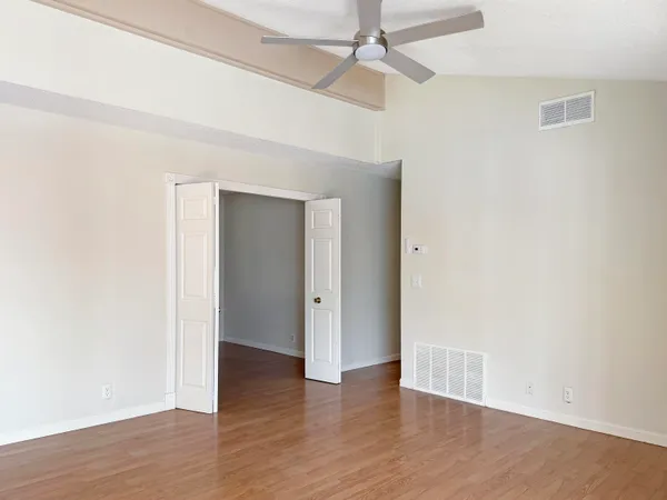 an empty room with wooden floor ceiling fan and windows