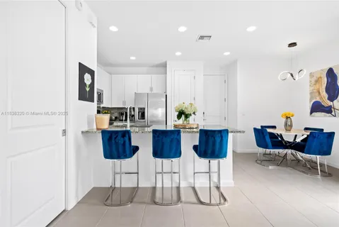 a kitchen with stainless steel appliances kitchen island granite countertop a dining table chairs and a refrigerator