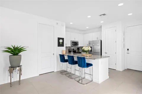 a kitchen with stainless steel appliances kitchen island granite countertop a refrigerator a stove a sink a dining table and chairs with wooden floor