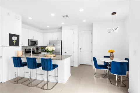 a kitchen with stainless steel appliances kitchen island granite countertop a dining table chairs and a refrigerator