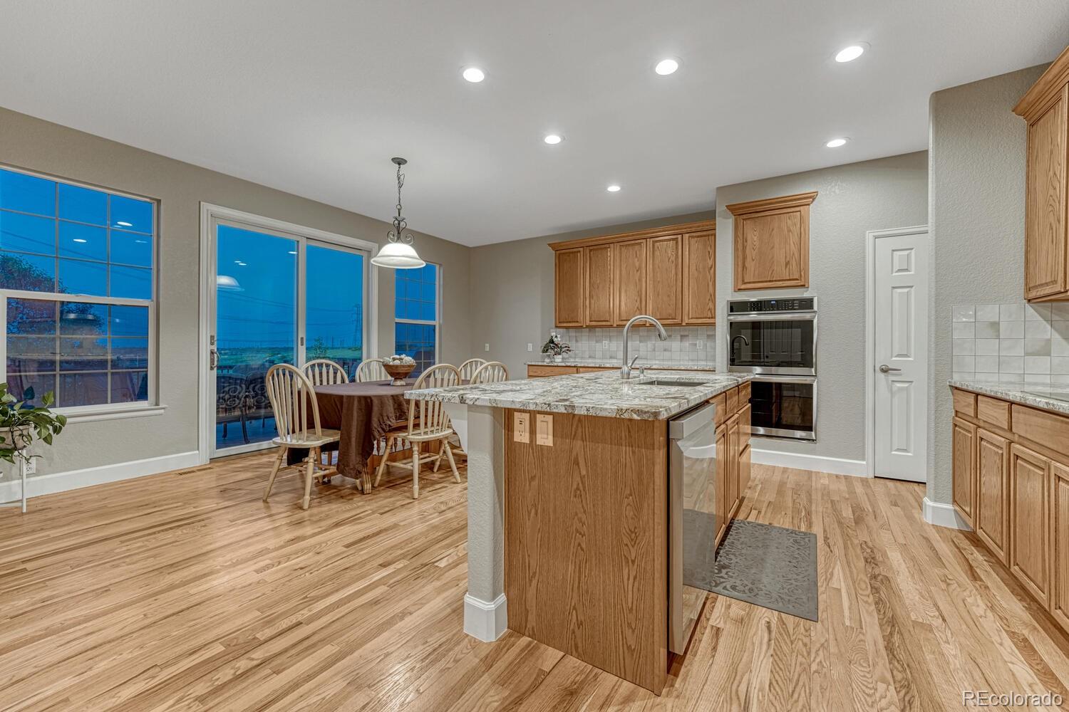 12350 Turquoise Terrace Street Castle Pines, CO 80108 - Photo 13 of 50 a kitchen with stainless steel appliances granite countertop a stove top oven a sink dishwasher a dining table and chairs with wooden floor