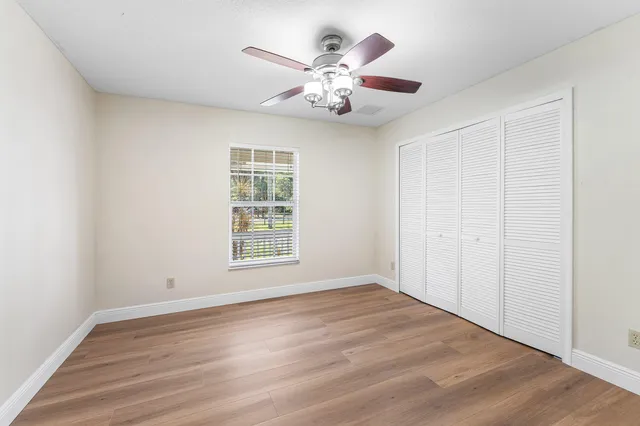 an empty room with wooden floor chandelier fan and windows