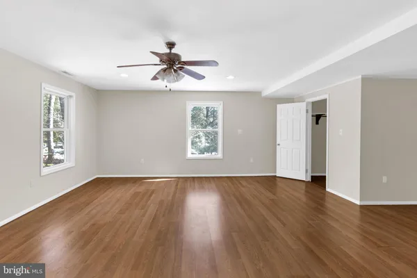 an empty room with wooden floor chandelier fan and windows
