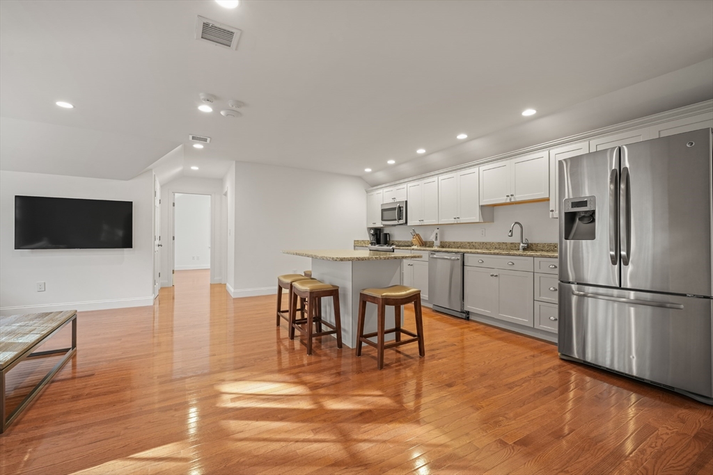 169 S Road Bourne, MA 02559 - Photo 41 of 42 a kitchen with stainless steel appliances kitchen island granite countertop a refrigerator a stove a microwave oven a dining table and chairs with wooden floor