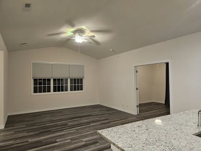 a view of an empty room with wooden floor and a chandelier fan