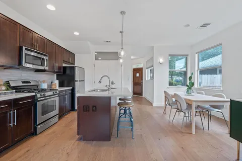 a kitchen with stainless steel appliances granite countertop a stove top oven a sink dishwasher a dining table and chairs with wooden floor