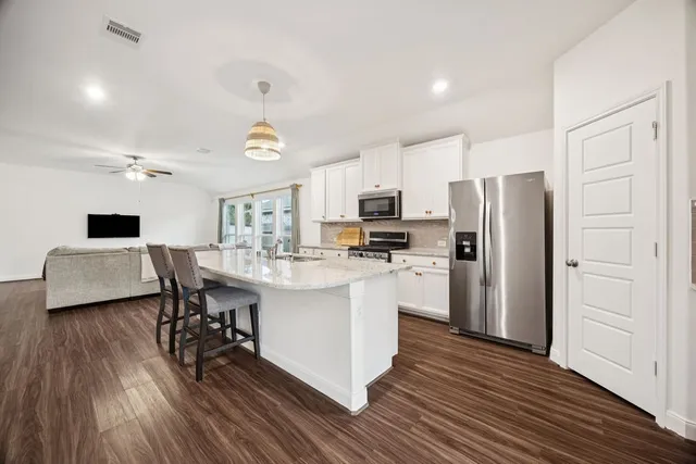 a kitchen with stainless steel appliances a refrigerator a stove a sink dishwasher and a dining table with wooden floor