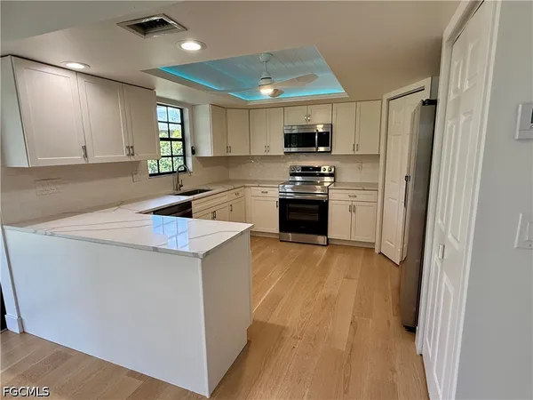 a kitchen with stainless steel appliances a refrigerator a sink dishwasher a stove and white cabinets with wooden floor