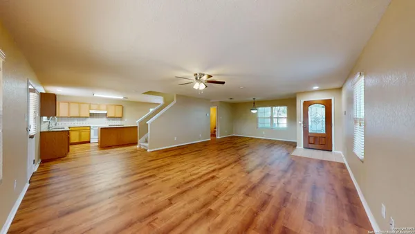 a view of an empty room with wooden floor and a kitchen