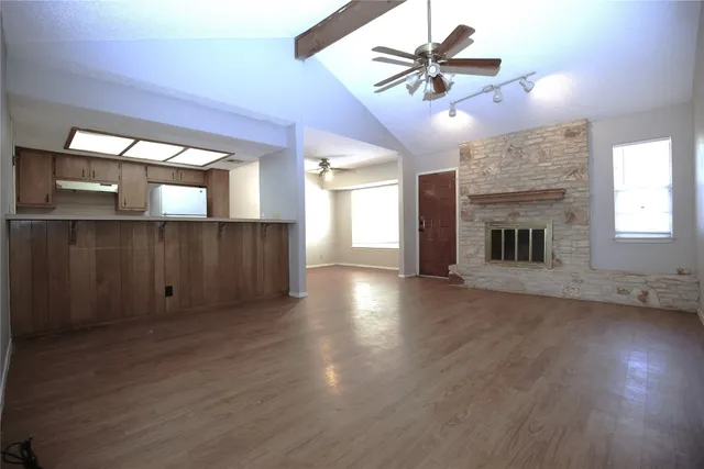 an empty room with wooden floor a ceiling fan and a kitchen view