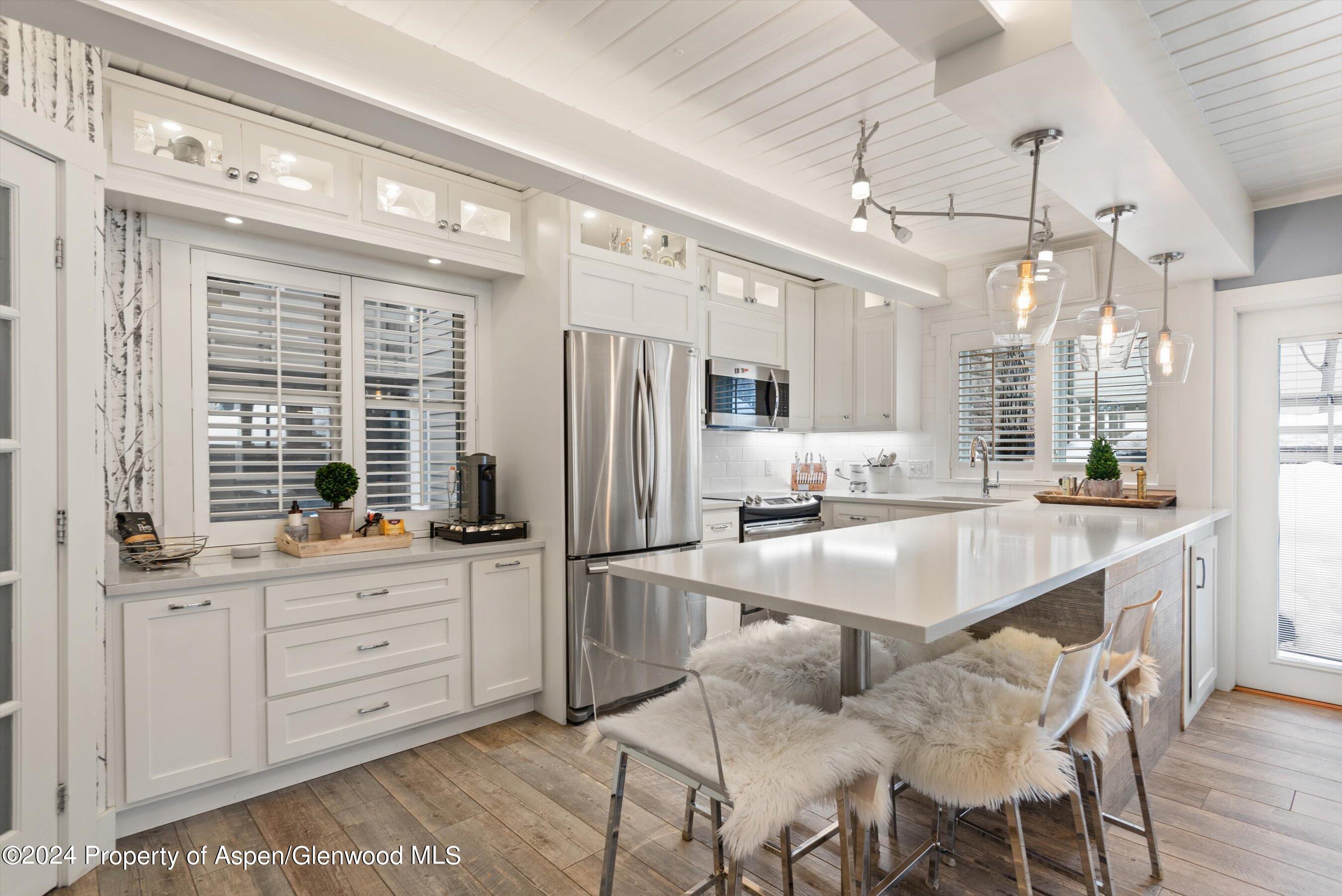825 East Hopkins Avenue, Unit 1N Aspen, CO 81611 - Photo 4 of 16 a kitchen with stainless steel appliances kitchen island granite countertop a refrigerator a sink dishwasher a dining table and chairs with wooden floor