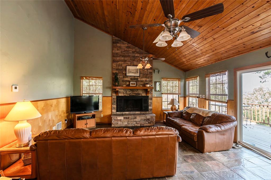 698 Storey Road Nocona, TX 76255 - Photo 22 of 34 Living area featuring wainscoting, wooden ceiling, a stone fireplace, wood walls, and stone finish floors