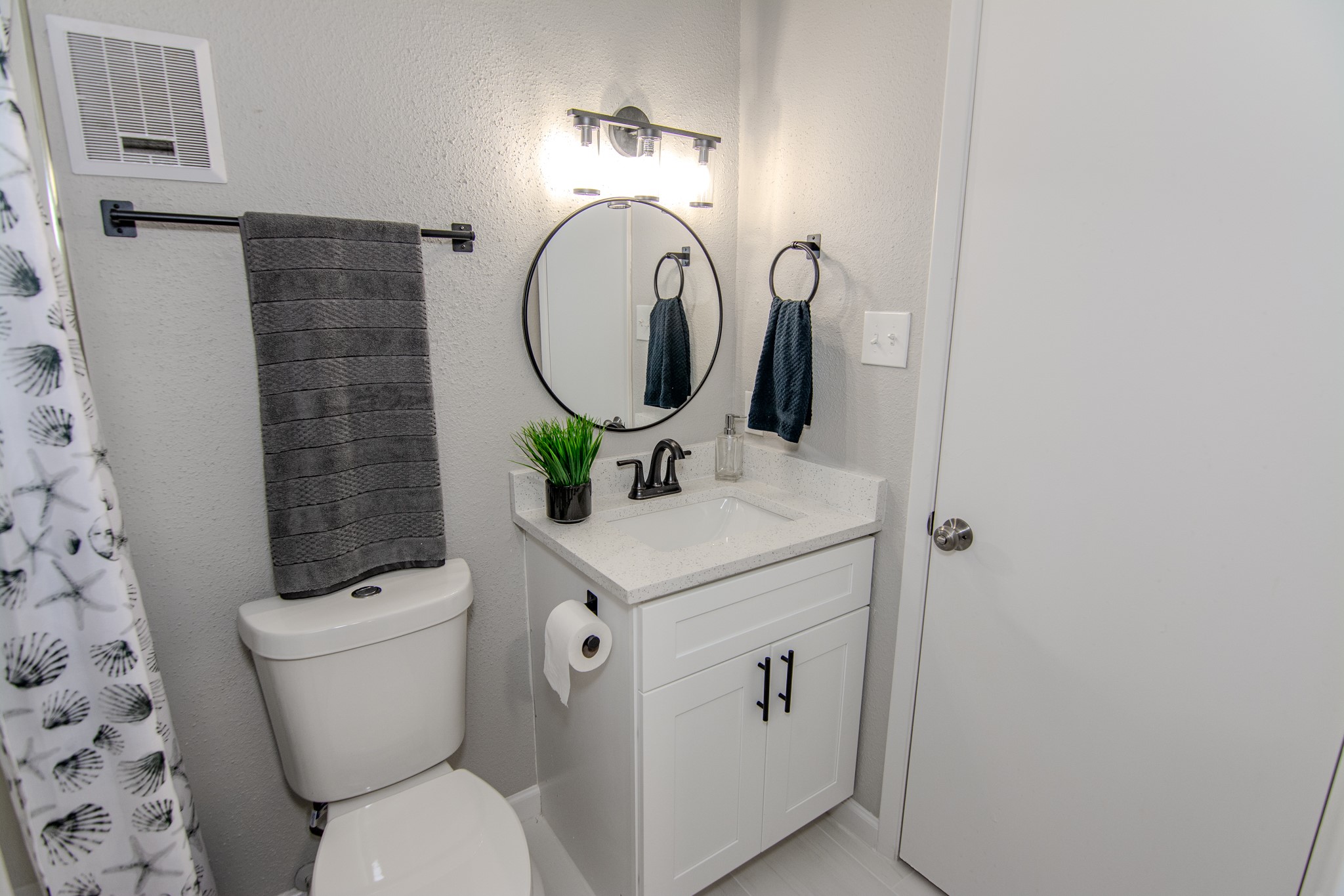 13009 Wirevine Lane Houston, TX 77072 - Photo 13 of 18 This modern bathroom features a sleek design with a round mirror, contemporary lighting, and a white vanity with a quartz countertop. It includes a toilet, towel rack, and stylish fixtures, offering a clean and functional space.