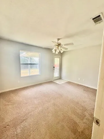 an empty room with a chandelier fan and windows