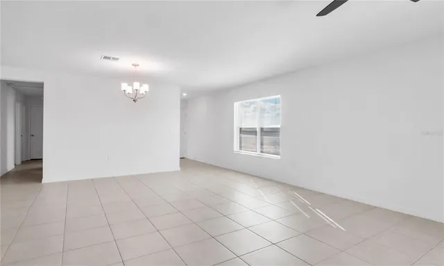 an empty room with chandelier fan and windows