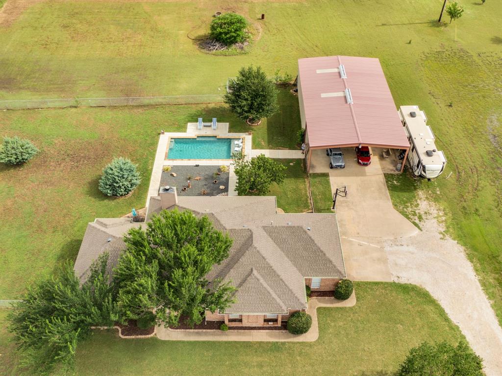 Brown-shingle roofline property featuring a rectangular pool with surrounding hardscaping, a detached carport, an expansive green lawn, and mature landscaping