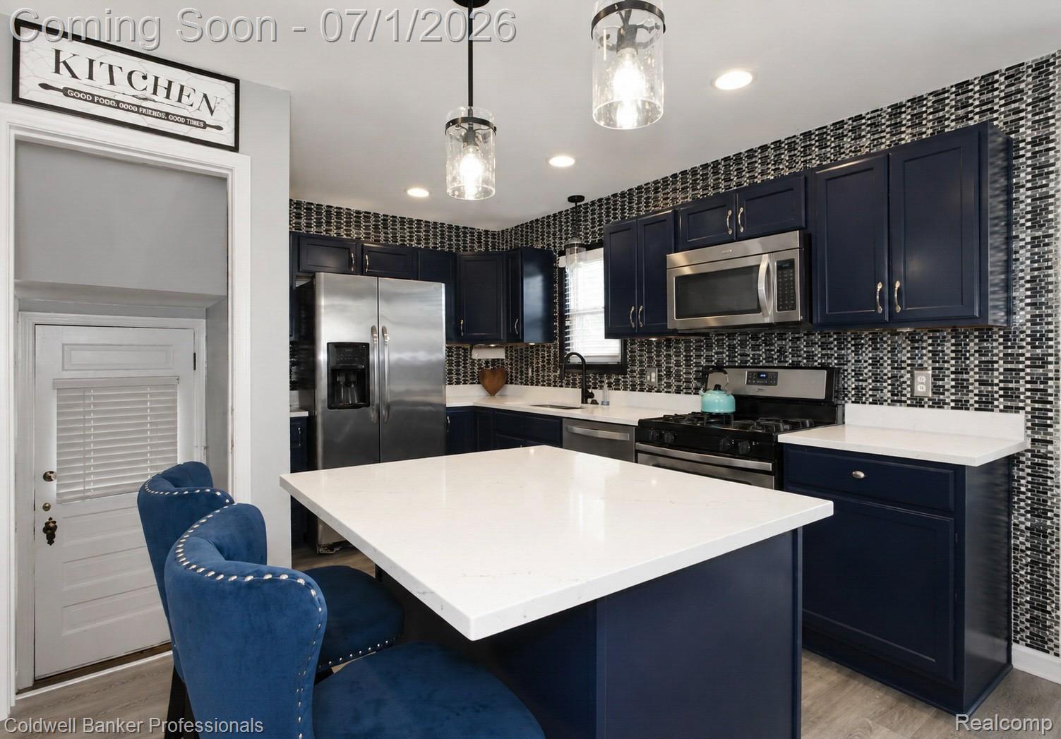 1168 Vernier Road Grosse Pointe, MI 48236 - Photo 17 of 32 Modern kitchen featuring a central island with a white countertop, dark blue cabinetry, stainless steel appliances, a patterned tile backsplash, and wood-finish flooring