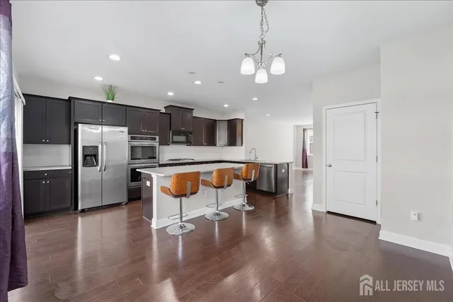 a kitchen with stainless steel appliances kitchen island granite countertop a refrigerator a stove a sink and a dining table with wooden floor