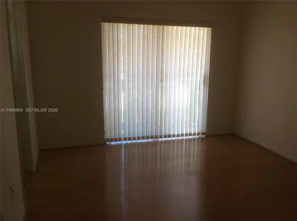 an empty room with wooden floor and windows with curtains