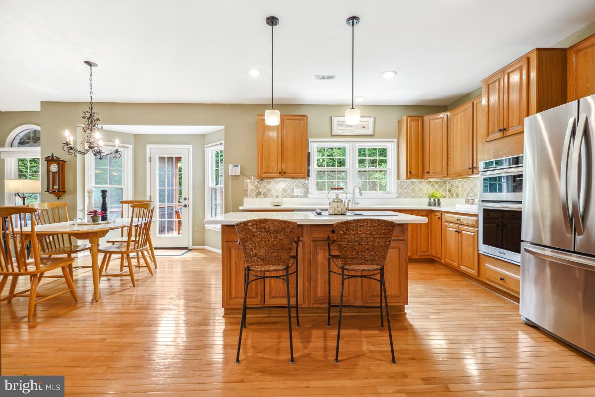 20479 Quarterpath Trace Circle Sterling, VA 20165 - Photo 4 of 41 a open kitchen with stainless steel appliances granite countertop a stove top oven a refrigerator a dining table and chairs with wooden floor