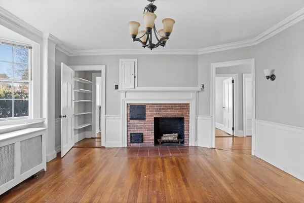 a view of an empty room with wooden floor fireplace and a window