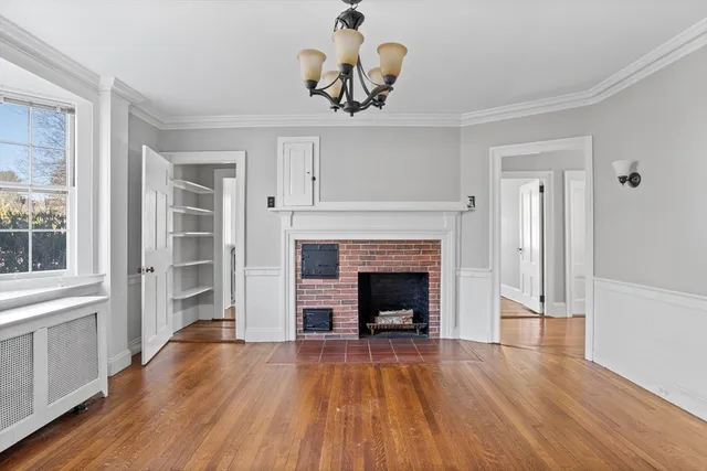 a view of an empty room with wooden floor fireplace and a window