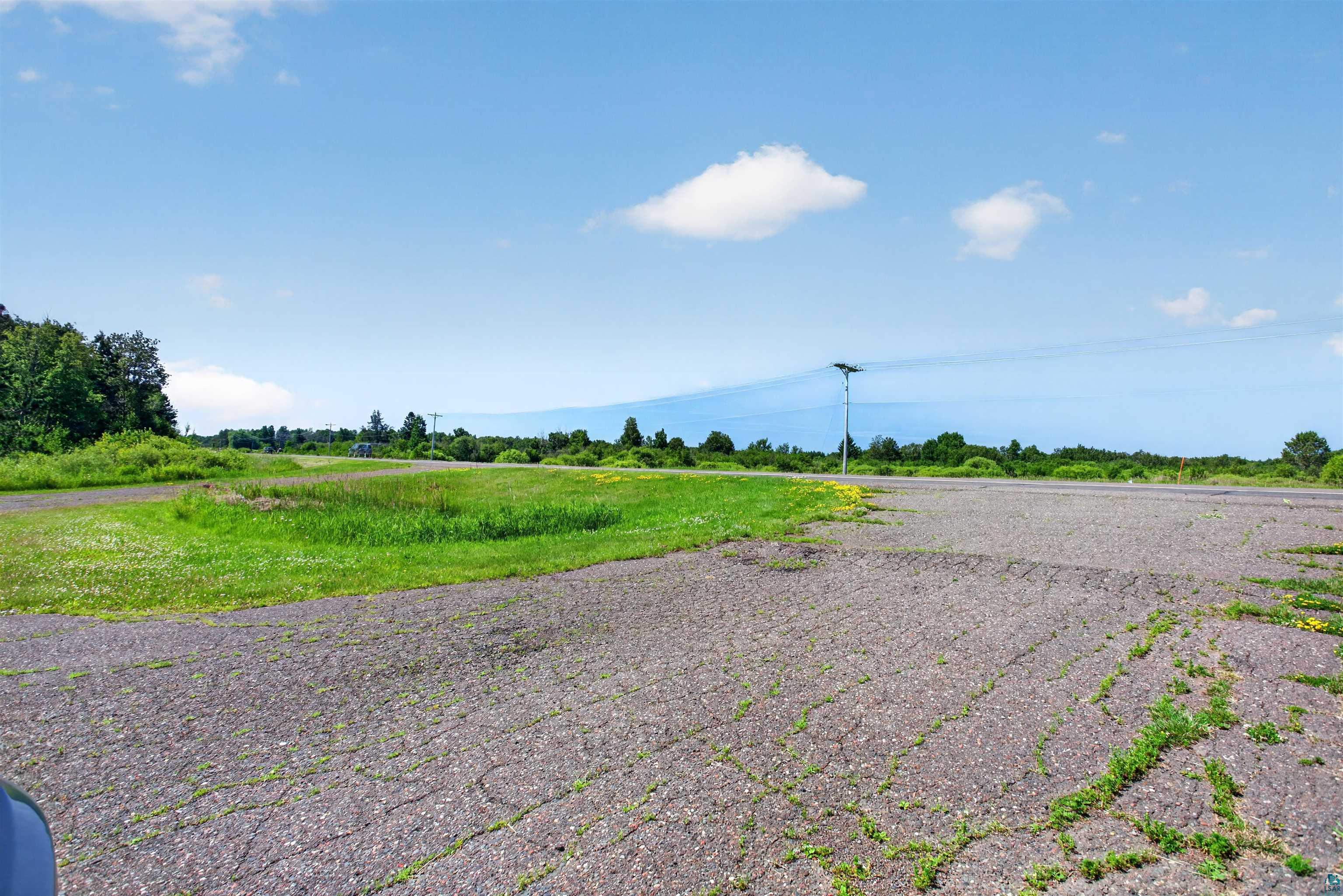 5868 Rice Lake Road Duluth, MN 55803 - Photo 38 of 39 Expansive asphalt surface with visible cracking, bordered by green grass and distant trees