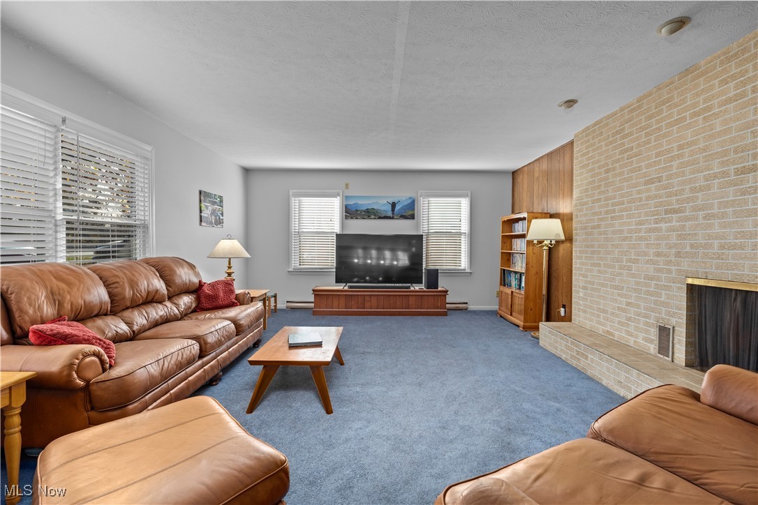 958 West River Road Vermilion, OH 44089 - Photo 4 of 40 Living room featuring a textured ceiling, baseboard heating, light carpet, and a brick fireplace