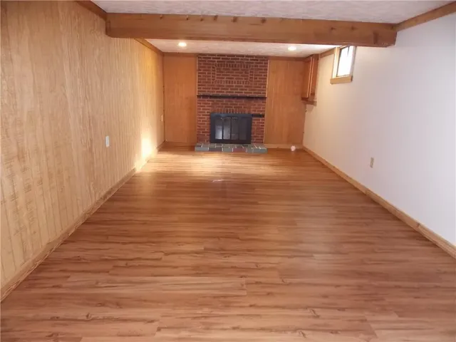 a view of an empty room with wooden floor fireplace and a window