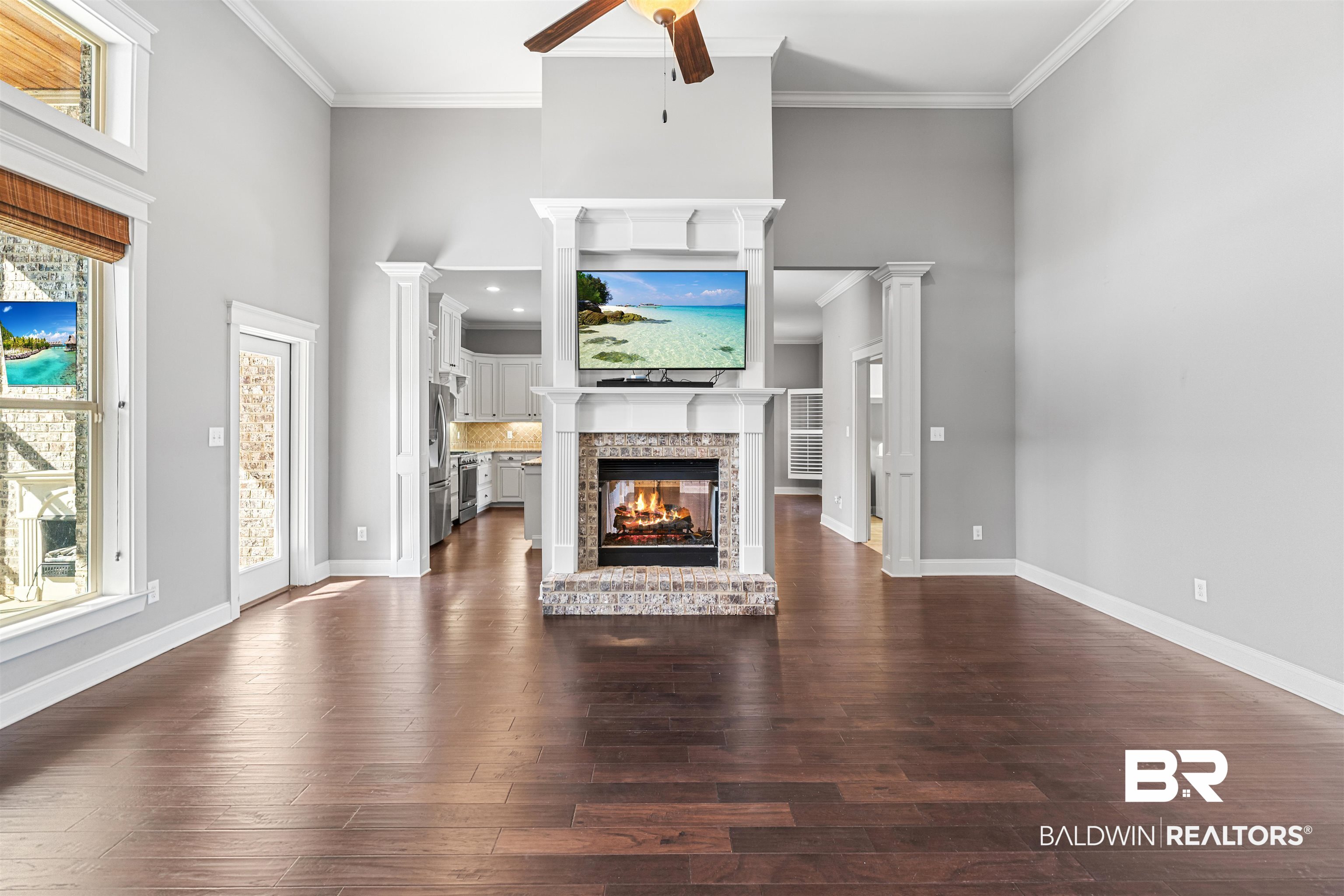 8844 Rosedown Lane Daphne, AL 36526 - Photo 3 of 24 Unfurnished living room with a multi sided fireplace, dark wood-style flooring, ceiling fan, crown molding, and a high ceiling