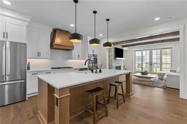 a kitchen with stainless steel appliances a stove a sink a refrigerator a center island a dining table and chairs with wooden floor