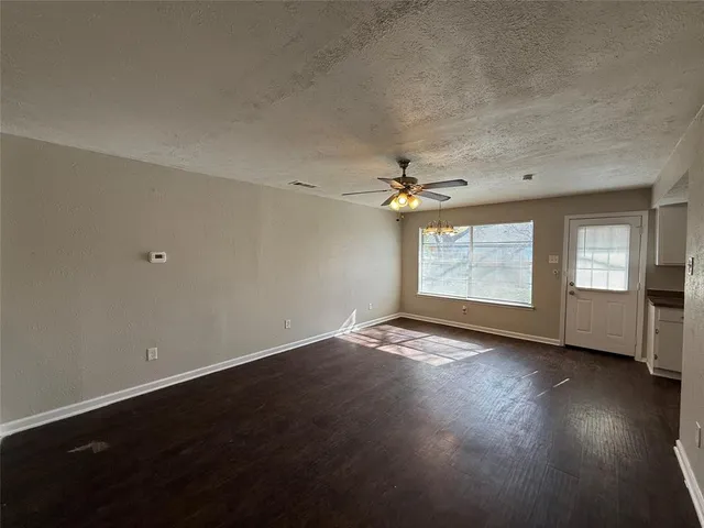an empty room with wooden floor chandelier fan and windows