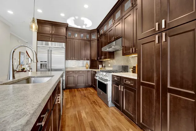 a kitchen with stainless steel appliances granite countertop a refrigerator a sink dishwasher a stove and a dining table with wooden floor