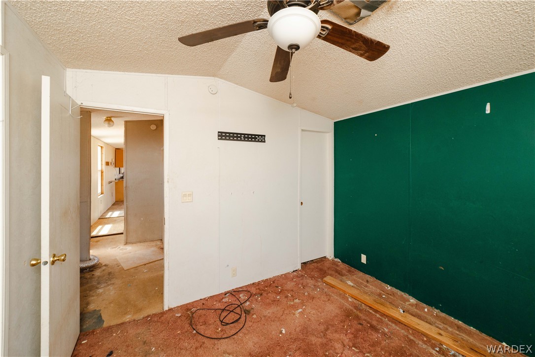 16435 South Wyatt Earp Road Yucca, AZ 86438 - Photo 12 of 57 Room featuring a textured ceiling with a ceiling fan, a partial accent wall in green, and a doorway opening to an additional interior space