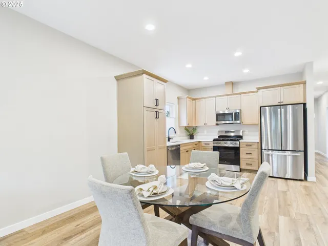 a kitchen with stainless steel appliances kitchen island granite countertop a refrigerator a stove a microwave oven a dining table and chairs with wooden floor