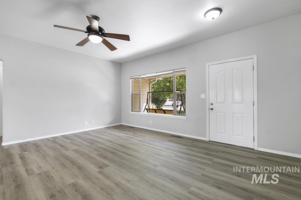 1183 Cortes Loop Twin Falls, ID 83301 - Photo 4 of 30 Spacious room featuring wood-finish flooring, a contemporary ceiling fan with integrated lighting, a white paneled entry door, and a large window providing outdoor views